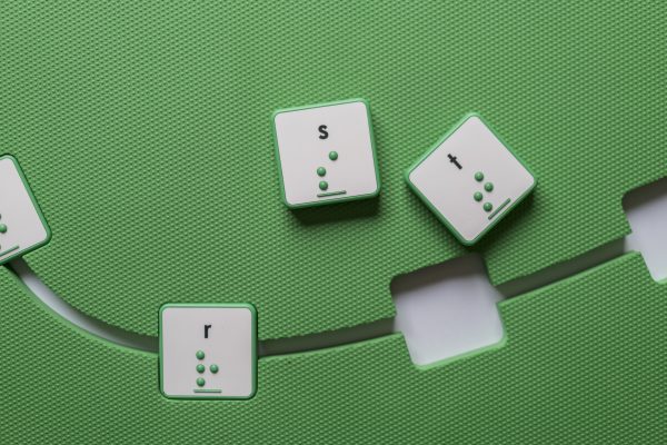 Overhead view of the green mat with square cut-outs and a few green square alphabet tiles.