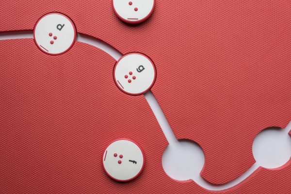 Overhead view of the red mat with circle cut-outs and a few red circular alphabet tiles.