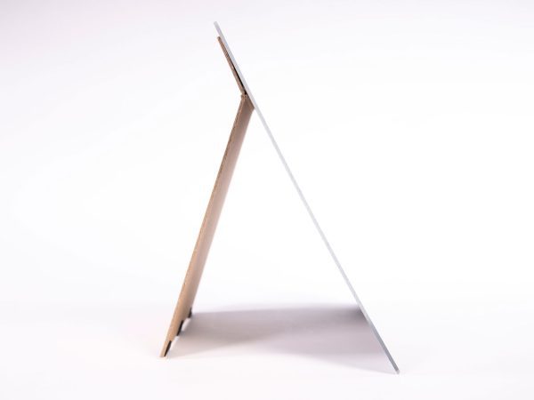 A side view of a frameless mirror propped up on a brown stand against a white background.