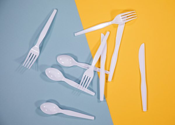 Three each of white plastic spoons, forks, and knives arranged on a yellow and light blue background.