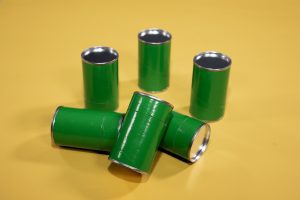 A set of six green cans with aluminum tops and bottoms arranged on a yellow background.