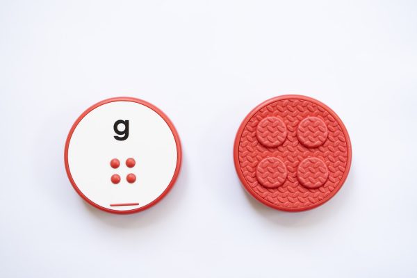 The front and back of a red, circular Reach & Match Alphabet Tile showing the letter g in print and braille.