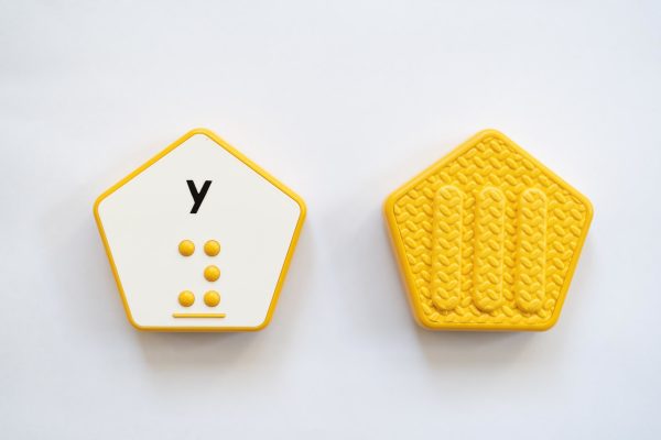 The front and back of a yellow, hexagonal Reach & Match Alphabet Tile showing the letter y in print and braille.