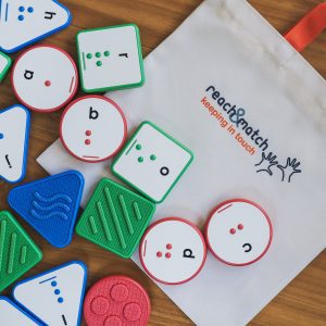 A variety of Reach and Match Alphabet Tiles laying on their canvas carrying case on a wooden floor.