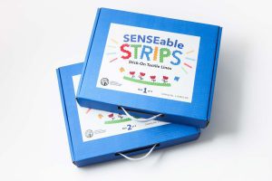 A top-down view of the two blue boxes included in the SENSEable STRIPS kit. In colorful graphic text, the label reads 