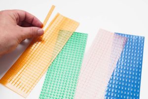 A hand separating one yellow dashed line path strip from the perforated set. Next to the dashed strips are dotted, greater-than, and railroad line path strips in green, clear, and blue.