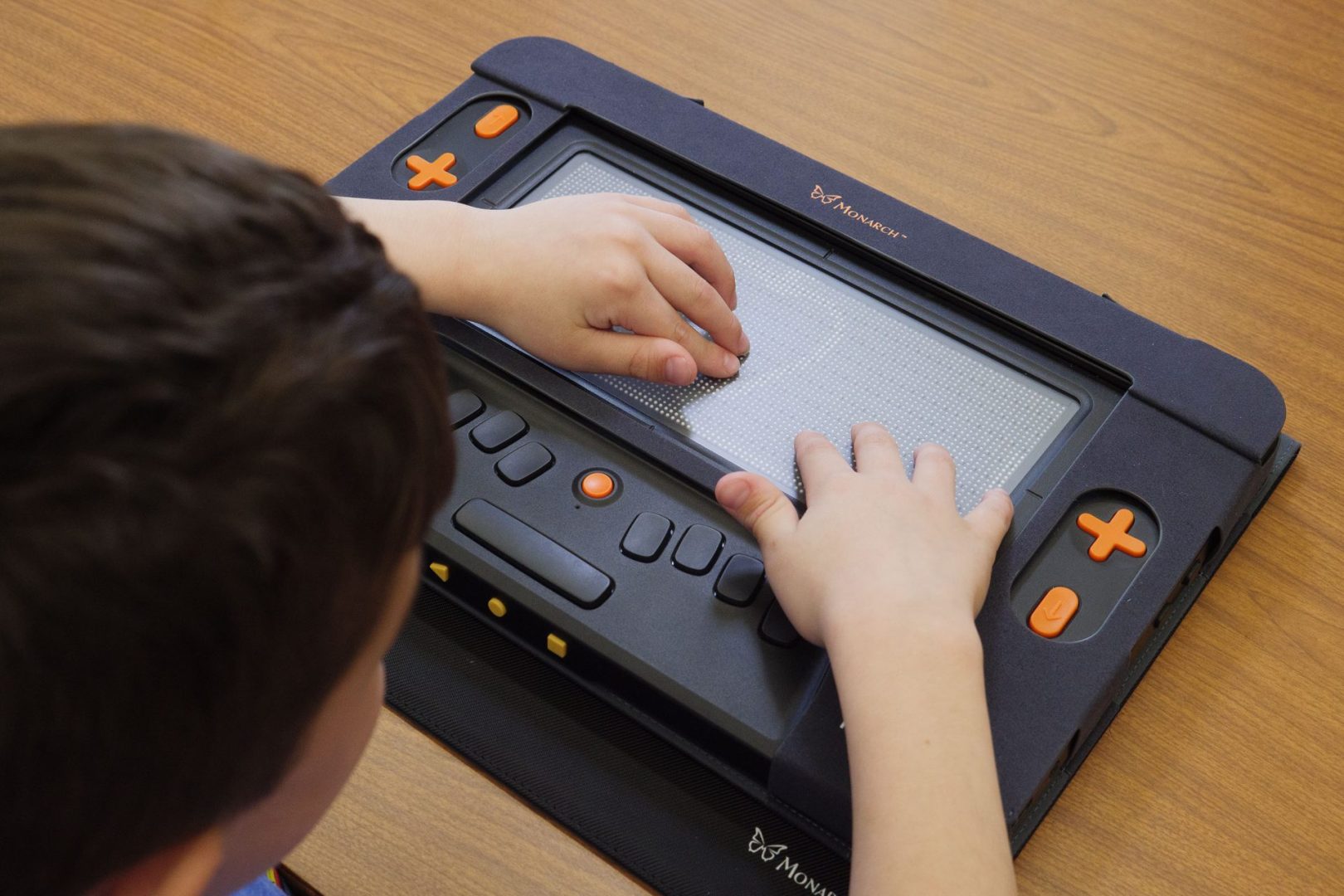 A student uses both hands to touch a tactile graphic of an apple displayed on the Monarch's multiline refreshable braille display.
