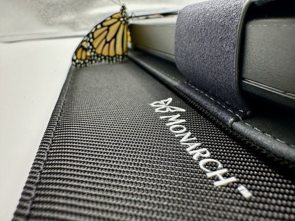 A close up of the Monarch logo on the bottom of the Monarch case with an orange Monarch butterfly sitting in the background.
