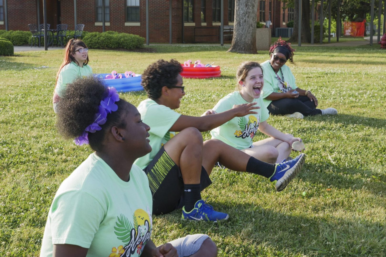 Four students sit outside on the grass laughing together.