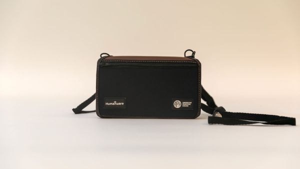 Front view of a closed turtleback case on a white background. The strap sits to the right of the device, and the cover has logos from HumanWare and APH.