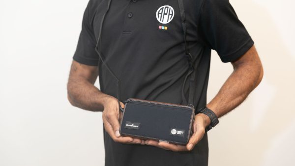 A man wearing a Chameleon cross body and holding the closed device with both hands. The front of the case contains logos for HumanWare and APH.