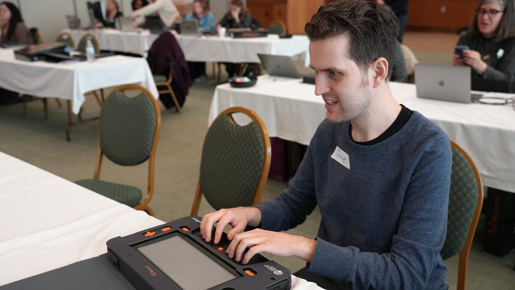 A young man wearing a gray sweater sits at a table typing on the Monarch.