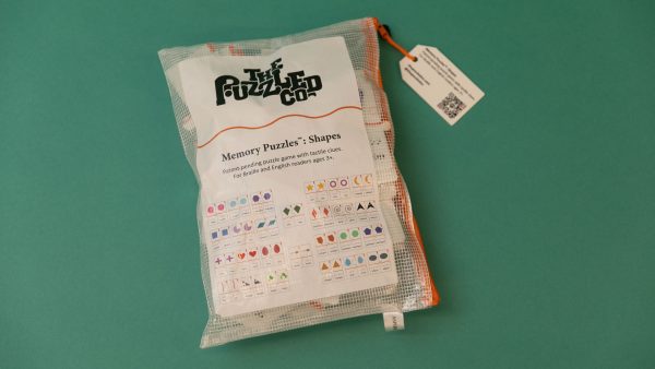 The Memory Puzzles: Shapes bag laid on a teal background. The sticker on the bag contains the Puzzled Company's logo as well as small graphics depicting the puzzle pieces in the kit.