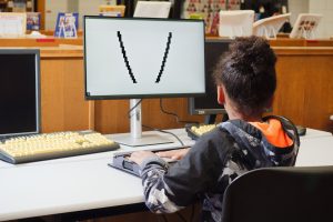 A student sits in front of a screen with a graph on it while placing their hands on the tactile graph on the Monarch in front of them.