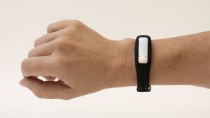 A wrist stretched across a white background wearing an OpticAware smart-watch style wearable. The device has a silver oval-shaped module fit into a black bracelet.