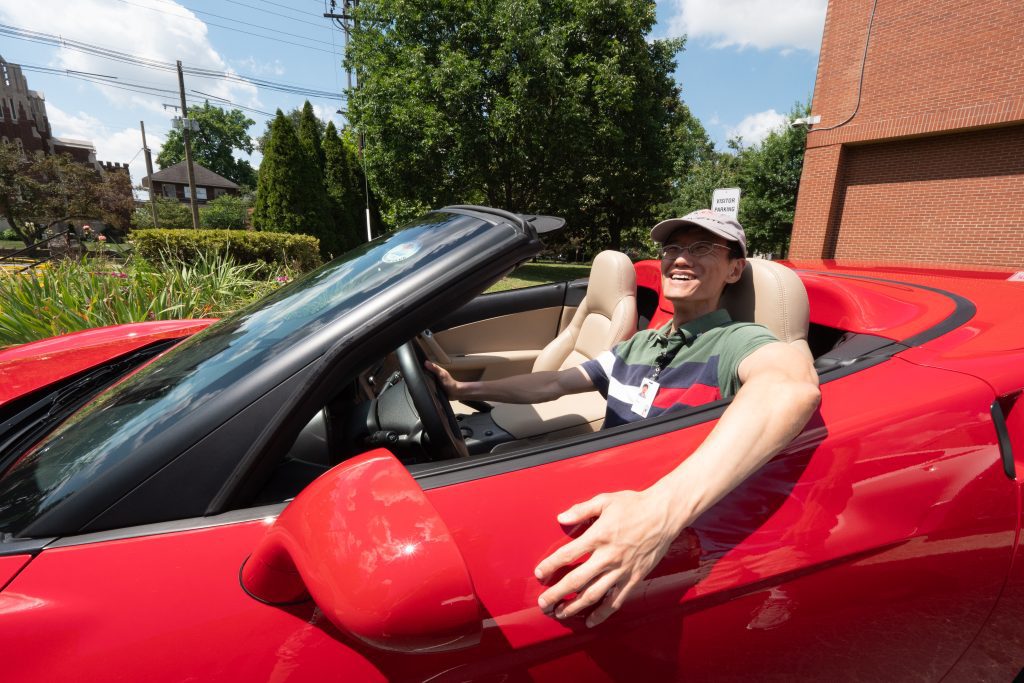 Man sits smiling in red Corvette.