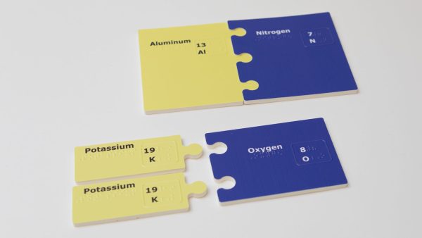 Two sets of bonded subunits on a white background. On top is a yellow Aluminum piece connected to a Nitrogen piece. Each subunit is printed and embossed with the element name, the atomic number, and the atomic symbol.