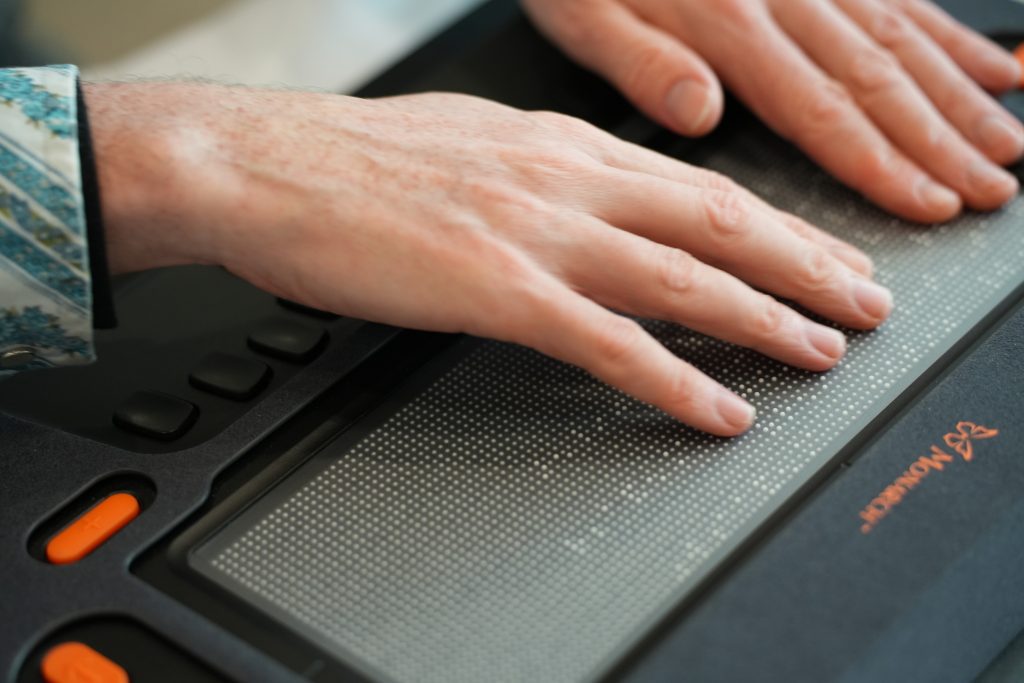 Two hands scanning lines of braille on Monarch’s multiline tactile display.