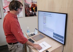 A ma stands in front of a TV screen wearing headphones.