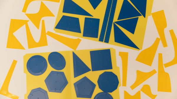 An overhead shot of the Geometric Drawing Stencils attached to a yellow folder with the 3D printed function stencils spread around them.