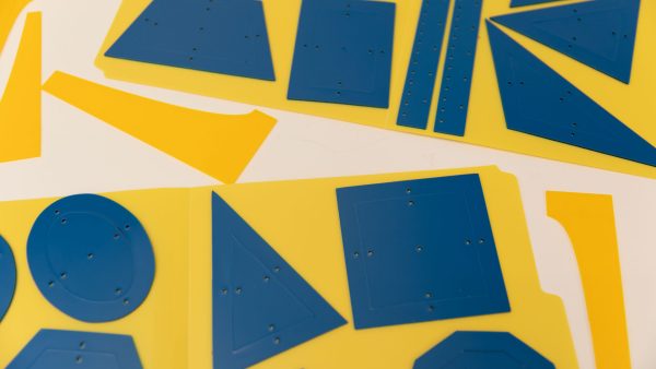 The Geometric Drawing Stencils on two yellow folders on a white background with 3D printed function stencils in between. Each blue stencil piece has tactile markings.