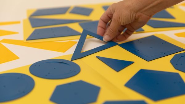 One hand holds an outer triangle stencil up. The inner triangle stencil is adhered to the yellow folder on a white background.