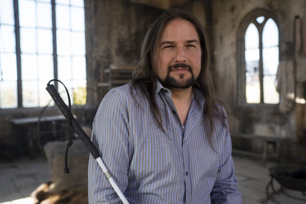 A man sits posing for his photo, smiling and holding a cane.