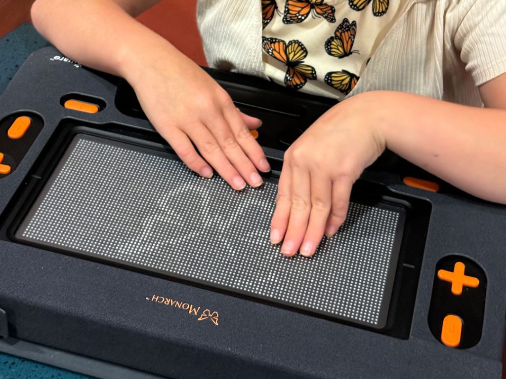 A young girl's hands feel the outline of a tactile butterfly on the Monarch.