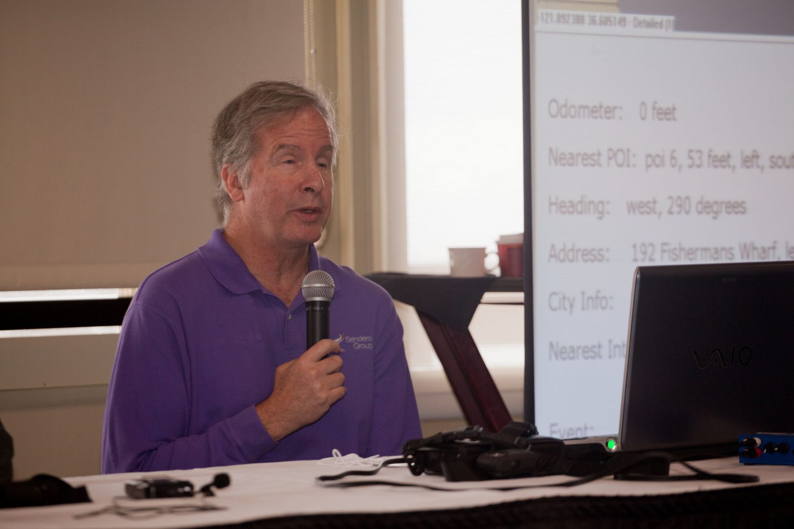 Mike sits at a desk, holding a microphone speaking during a presentation.