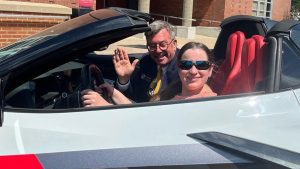 Jessica Minneci sits in a Corvette with Brian Baker waving. 