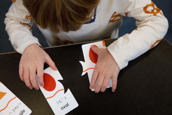 A preschool aged boy in a white shirt with pretzel graphics on it plays with two oval Memory Puzzle pieces.