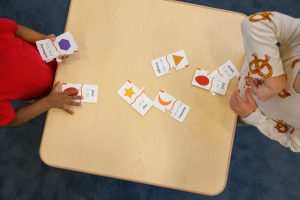 An overhead shot of two preschoolers playing with the Memory Puzzle pieces on a wooden table.