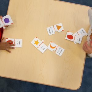 An overhead shot of two preschoolers playing with the Memory Puzzle pieces on a wooden table.