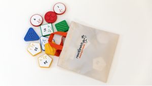 Number tiles of different shapes and colors lay on a table, coming out of a tan bag.