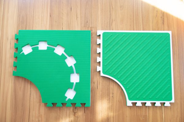 Two green Reach & Match mats side by side demonstrating the differences between the textured side and the side with square cut-outs for tiles and a traceable path.