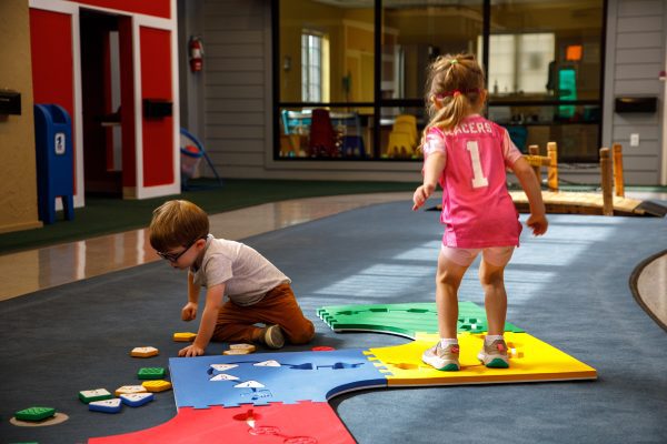 A Reach and Match Light kit assembled on the ground in a path with a little girl jumping along the squares and a little boy playing with tiles on the floor.