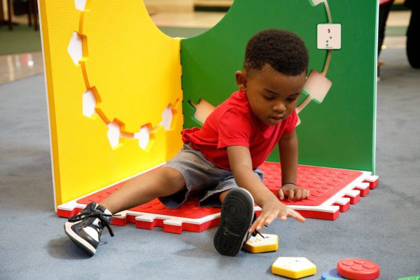 A little boy sitting on the Reach and Match Light kit with the tiles assembled vertically. He is reaching for a yellow tile.