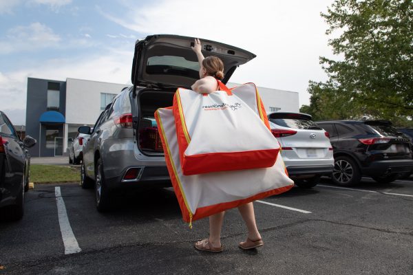 A woman holding the smaller Reach and Match Light kit on her shoulder on top of the original kit to show how much smaller the new kit is. She is reaching to close the back latch of a van.