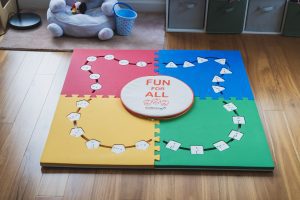 All four pieces of the Reach & Match Light kit assembled in a square on a wooden floor with alphabet tiles inserted into the cut-outs. The carrying case sits in the center and reads 