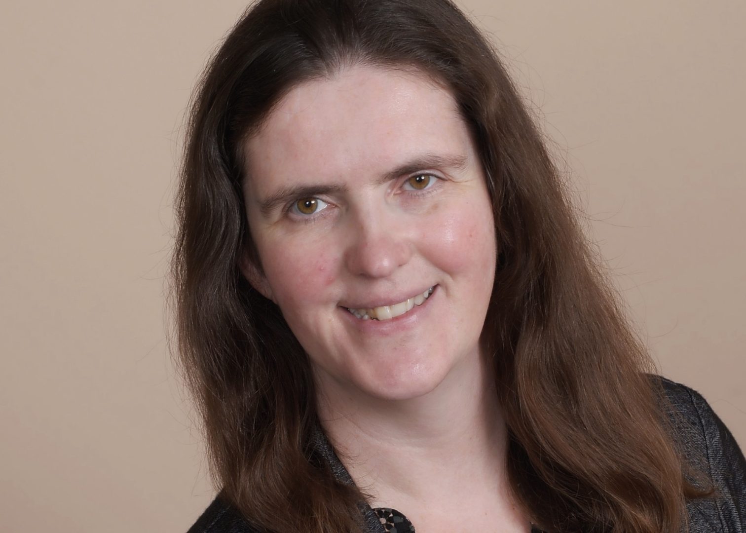 Gina smiles at the camera in front of a plain background.