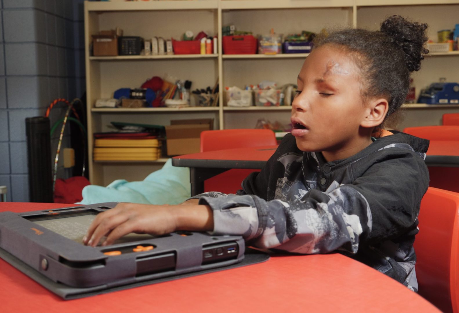 A young girl reaches her arms out to feel the refreshable braille and explore her Monarch.