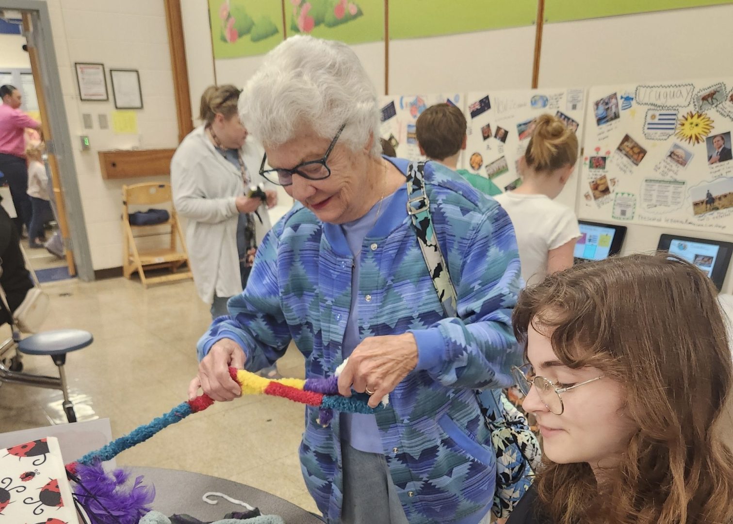 A young woman sits and weaves, while an older woman stands weaving next to her.