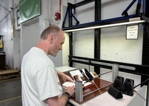 Joey stands in front of desk station, with his hand on a book, while a smartphone reads aloud the text.