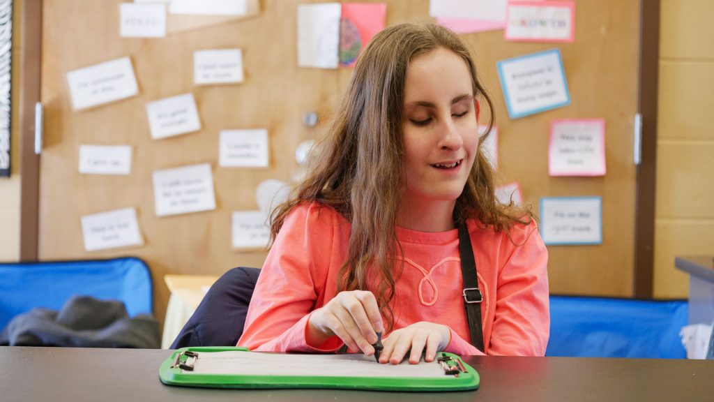 A girl with brown hair, in a pink shirt, drawing on a tactile doodle sheet