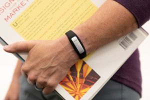 A woman's hand holding a closed book with an OpticAware band on her wrist.