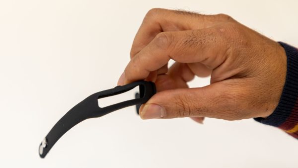 A man's hand holding an unfastened black replacement OpticAware band with the center module missing.