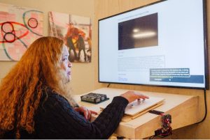 A woman sits at a computer, looking back over her shoulder at the camera.